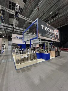 Stoisko targowe Technica prezentuje sprzęt kuchenny , w tym urządzenia i maszyny ze stali nierdzewnej. Duże tablice reklamowe przedstawiają nazwę marki. Stoisko jest wyposażone w lady, wyświetlacze produktów i oświetlenie, ustawione w przestronnej hali z wysokim sufitem przemysłowym. to kongres szefów kuchni i restauratorów. projekt i nadzór Tatjana Kobuszewska trksystem.com