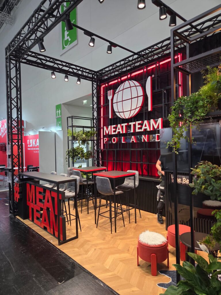 Stoisko targowe MEAT TEAM POLSKA na targach Anuga 2025 Kolonia to Rama z czarnego systemu quadro jako szkielet stoiska, zaprojektowana przez Tatjanę Kobuszewską przy użyciu TRK System, z odważnym brandingiem, czerwonymi neonowymi akcentami i nowoczesnym wystrojem. projekt i nadzór Tatjana Kobuszewska