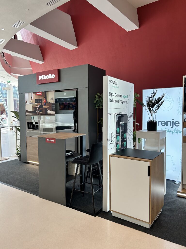 Mikro stoisko Miele prezentuje eleganckie piekarniki w czarnej szafce ze stołem barowym i stołkami. Na dniach designu interioro, Projekt Tatjany Kobuszewskiej, TRK System.