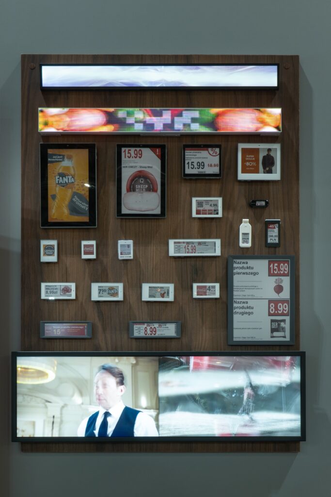 Na targach Retail Show 2024 drewniany panel prezentuje cyfrowe metki cenowe, zdjęcia produktów oraz ekrany. Ekspozycja, stworzona przez firmę Iglootechnika, zawiera pikselowy obraz umieszczony w górnej części panelu oraz prezentuje innowacyjne elementy kasetonowe z folii 3D. projekt i nadzór Tatjana Kobuszewska