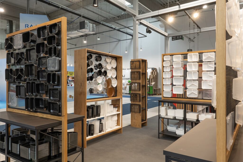 Showroom prezentuje różne pojemniki kuchenne na drewnianych półkach i metalowych stojakach. Oprócz nowoczesnego układu, rodowe sztućce są elegancko zaaranżowane, odzwierciedlając wyrafinowany styl widoczny w stoisku targowym Bittner podczas Warsaw Pack. projekt i nadzór Tatjana Kobuszewska