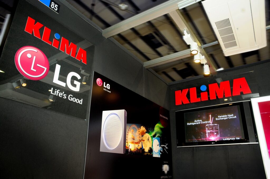 Na stoisku wystawowym firmy LG widnieją duże logo KLIMA i LG Life’s Good, klimatyzatory oraz telewizor prezentujący funkcje produktów. Niestandardowe wykorzystanie systemu Octanorm — architektoniczna kompozycja — wzbogaca tę przestrzeń o charakterze technologicznym dzięki czarnym ścianom i oświetleniu sufitowemu. projekt i nadzór Tatjana Kobuszewska
