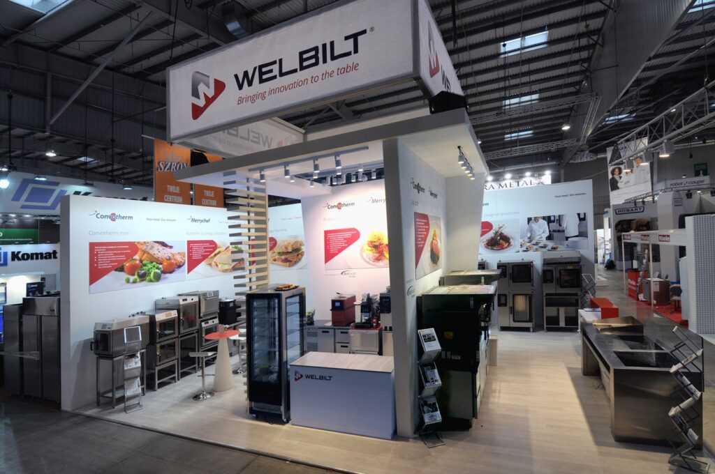 Na targach Eurogastro 2017 stoisko firmy Welbilt prezentuje sprzęt kuchenny, duże tablice ekspozycyjne z obrazami potraw oraz hasło „Bringing innovation to the table”. Jasno oświetlone stoisko wyróżnia się spośród innych stoisk wystawowych w przestronnej hali. projekt i nadzór Tatjana Kobuszewska