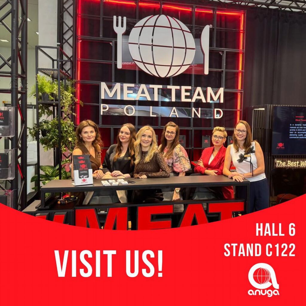 Za ladą na stoisku Meat Team Polands stoi sześć uśmiechniętych kobiet, a za nimi widnieje duże logo oraz symbol przedstawiający przybory kuchenne. Stoisko ma nowoczesny, czerwono-czarny wygląd. Napis brzmi: ODWIEDŹ NAS W HALI 6, STOISKO C122 na targach anuga... projekt i nadzór Tatjana Kobuszewska