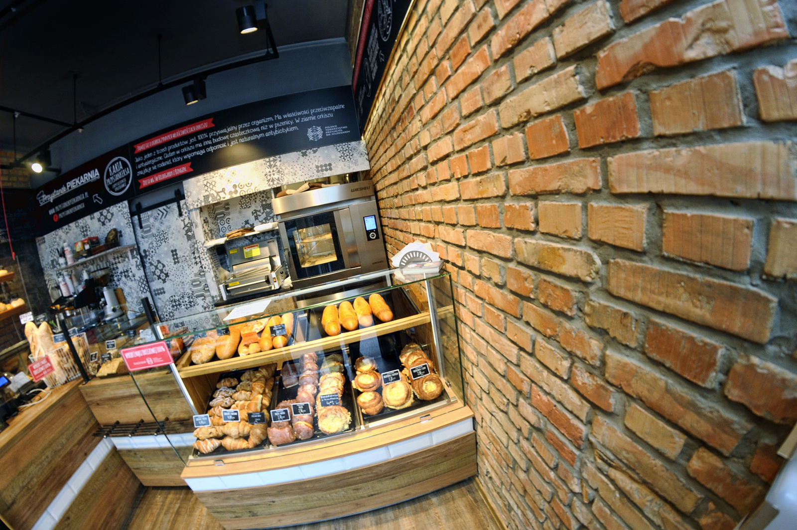 Lada piekarni z jasnego dębu przy odrestaurowanej ścianie z cegły, z witryną na pieczywo i koszami. projekt i nadzór Tatjana Kobuszewska trksystem.com