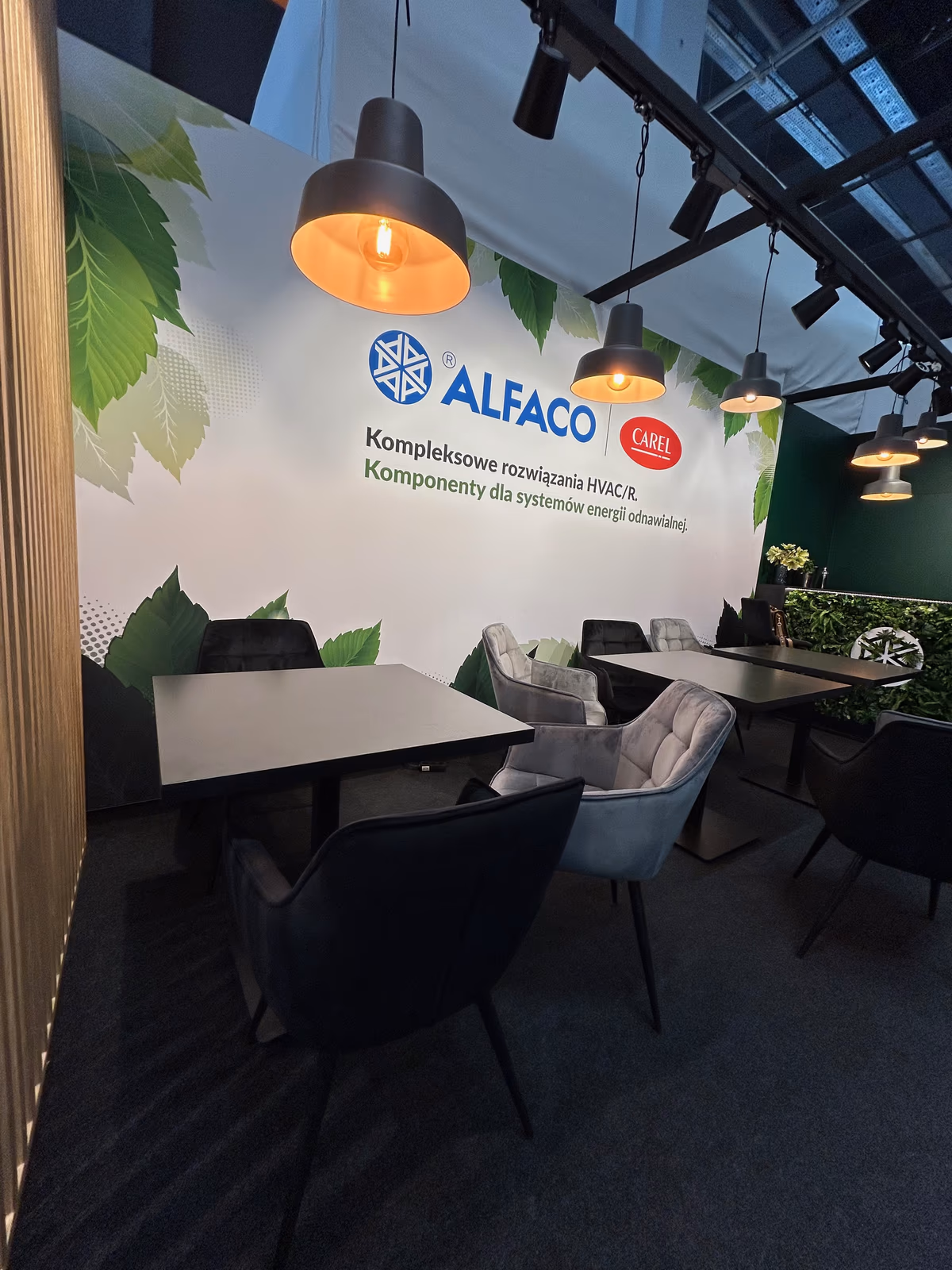 Strefa rozmów na stoisku Alfaco: ciemnozielone ściany, grafika z liśćmi i lampy nad stolikami