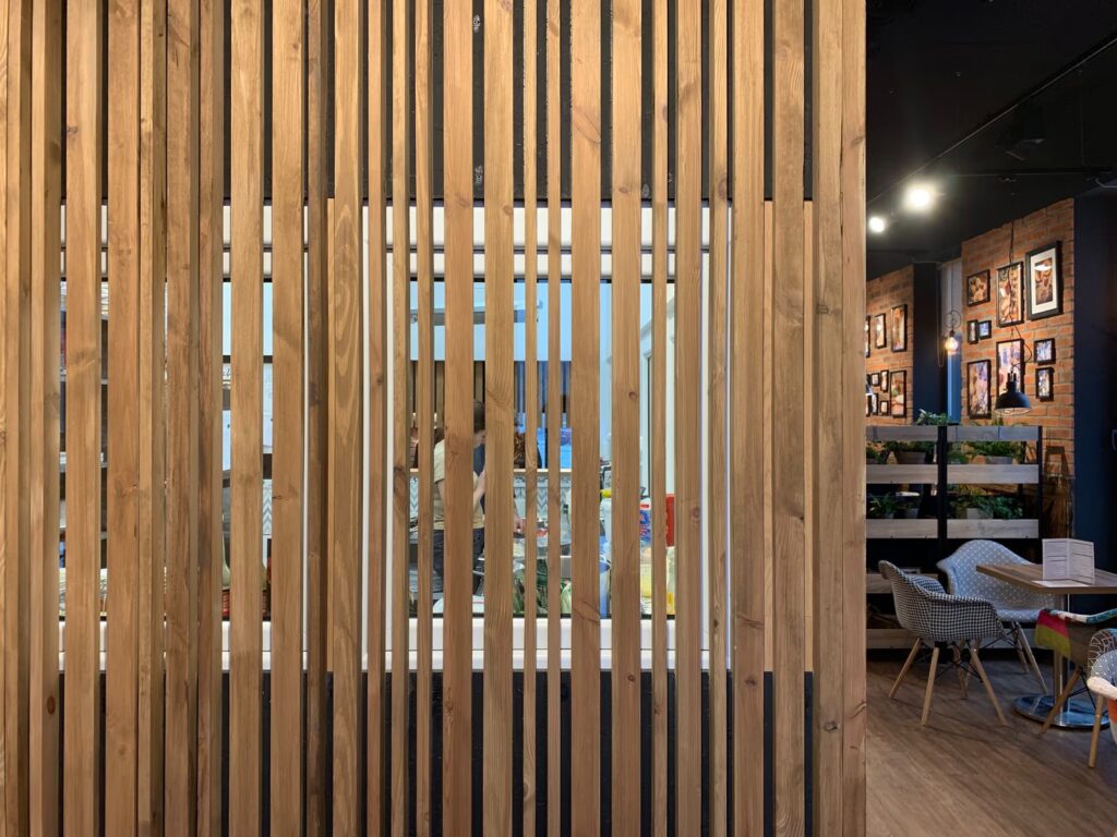 Ażurowy ekran z pionowych drewnianych lameli oddzielający salę konsumpcyjną od zaplecza kuchennego w bistro Przystanek Piekarnia w Piasecznie. projekt i nadzór Tatjana Kobuszewska trksystem.com