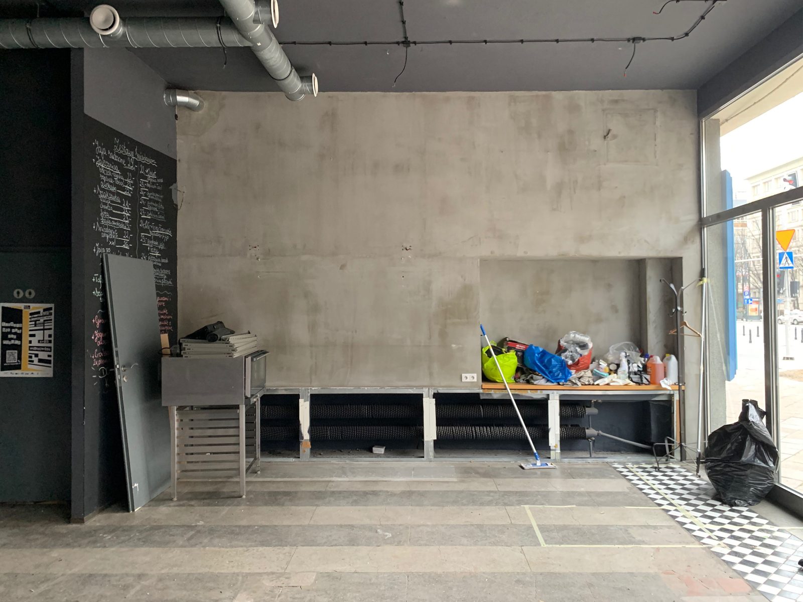 Wnętrze po demontażu: szare ściany, odsłonięte instalacje pod sufitem i surowa posadzka