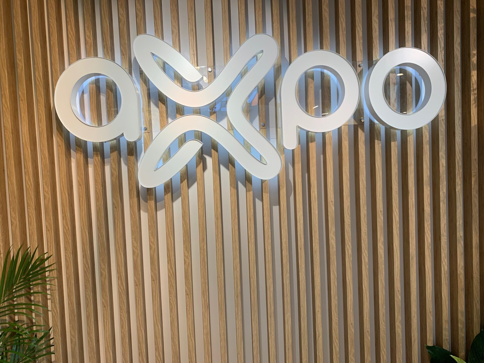 Drewniana ściana z przestrzennym, podświetlanym logo Axpo w nowej identyfikacji