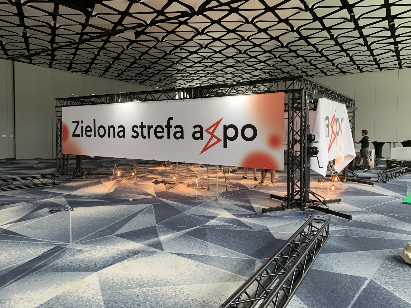 Kratownica z podświetlanym napisem Zielona strefa axpo nad stoiskiem konferencyjnym