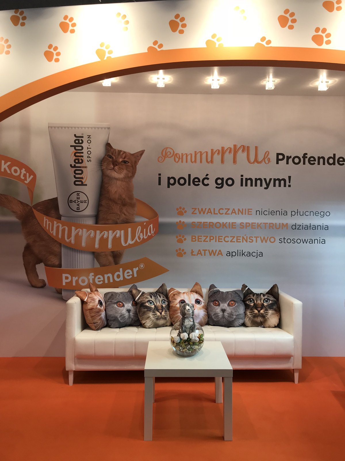 Biała kanapa z poduszkami w kształcie kocich głów pod grafiką z kotem i tubką Profender