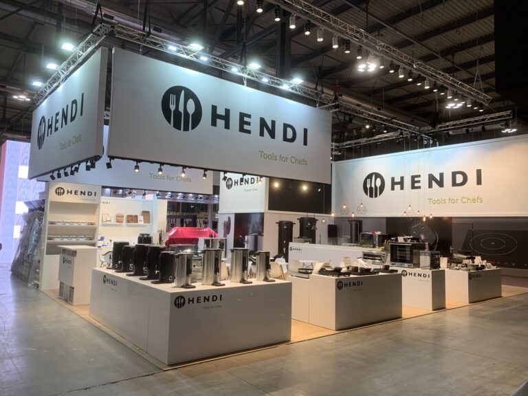 Duże białe stoisko z czarnym fryzem i logo Hendi, wzdłuż lad ekspozycja sprzętu gastronomicznego