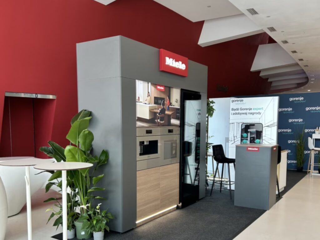 Kraków mini stoisko Miele Kompaktowe stoisko wystawowe marki Miele z wbudowanym sprzętem kuchennym, ekspresem do kawy i roślinami.