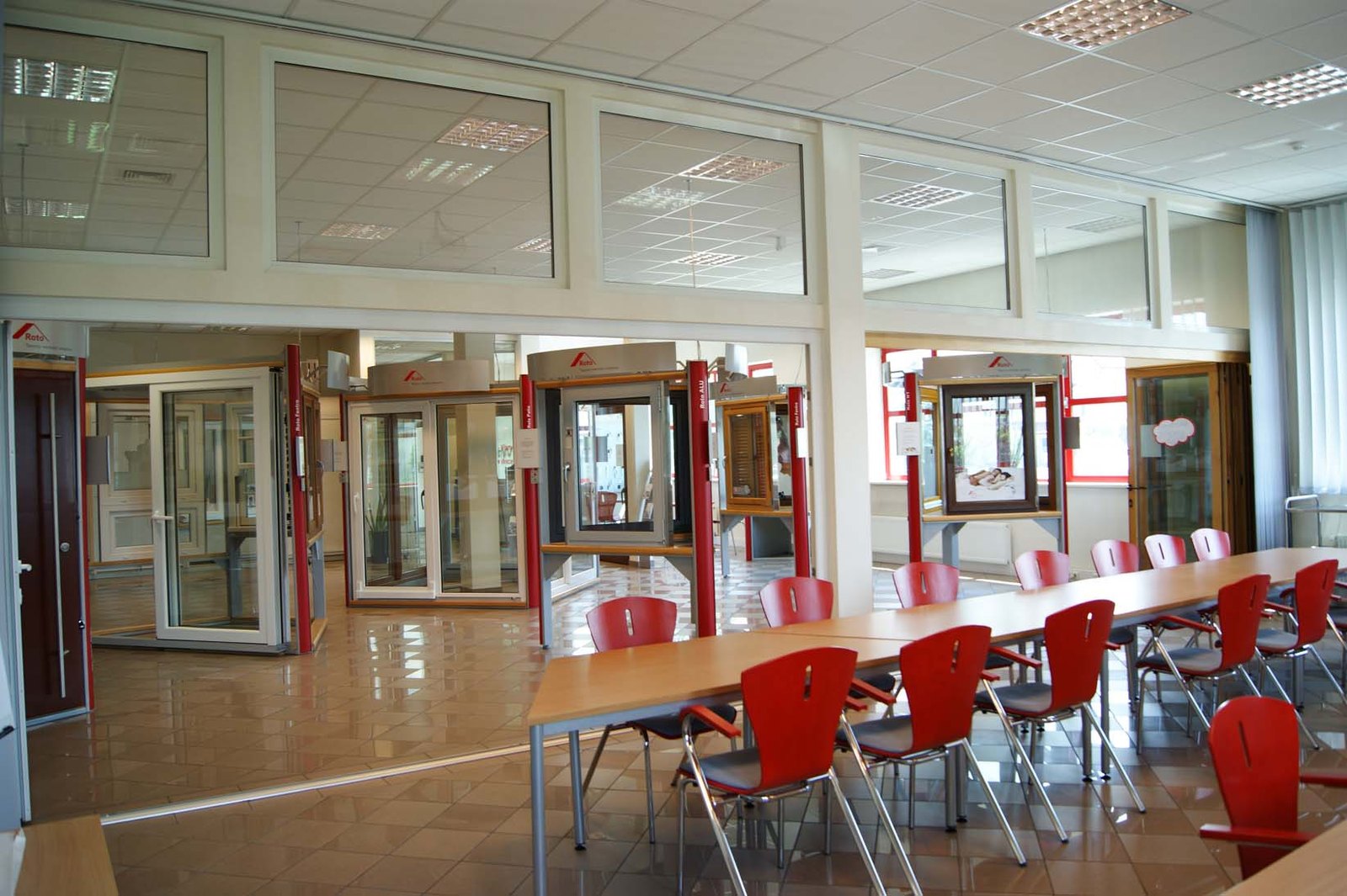 Sala szkoleniowa z długim stołem i czerwonymi krzesłami, obok ekspozycja okien