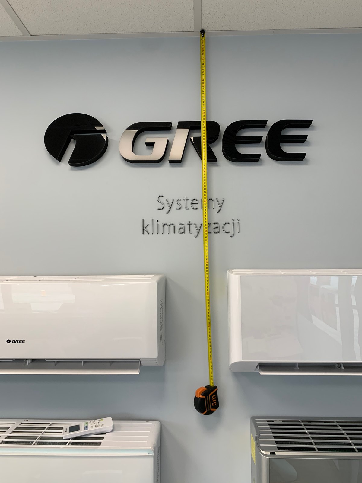 Miara zwijana przy logo Gree na ścianie podczas inwentaryzacji przed projektem ekspozycji