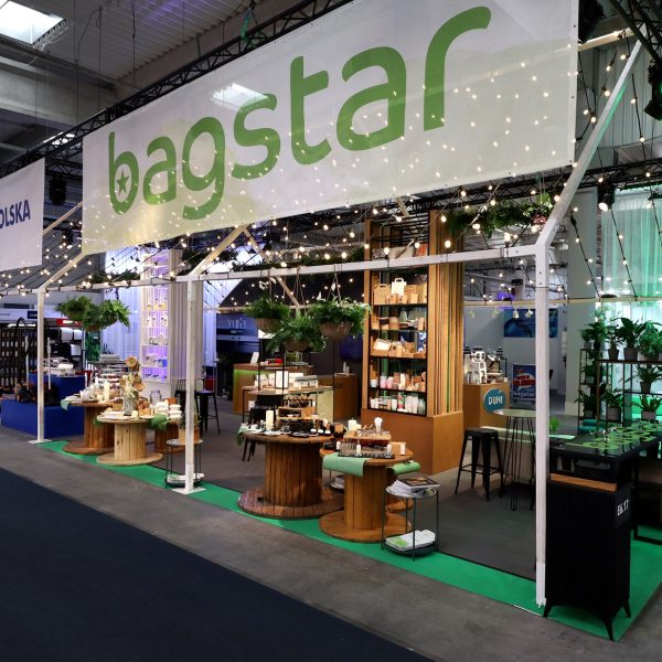 Stoisko targowe Bagstar z dużym białym szyldem, lampkami sznurkowymi, zielono-białym wystrojem i ekspozycją różnych produktów na drewnianych stołach - idealne dla osób zainteresowanych stoiskiem targowym w pytaniach i odpowiedziach. Zieleń dodatkowo zachęca do odwiedzin. Targi EuroGastro, Ptak Warsaw Expo.projekt i nadzór Tatjana Kobuszewska trksystem.com