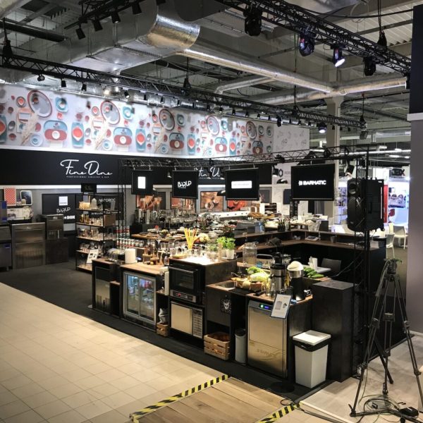 Nowoczesny showroom kuchenny zaprojektowany przez projekt i nadzór Tatjana Kobuszewska trksystem.com, wyposażony w powierzchnie ze stali nierdzewnej, półki na szkło, kolorowy mural na ścianie oraz górne kanały przemysłowe zapewniające stylową i funkcjonalną ekspozycję. projekt i nadzór Tatjana Kobuszewska trksystem.com