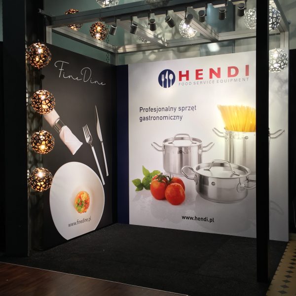 Stoisko targowe prezentuje banery "FineDine" i "Hendi Food Service Equipment". Jedna strona przedstawia wykwintny talerz, widelec i nóż, a druga garnki ze stali nierdzewnej, pomidory i makaron. Nad nimi wiszą ozdobne kuliste lampy. projekt i nadzór Tatjana Kobuszewska trksystem.com