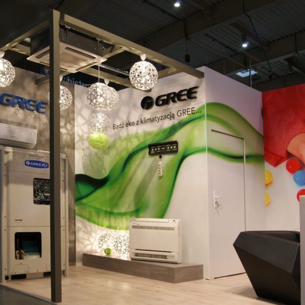 Na nowoczesnym stoisku targowym firmy GREE można zobaczyć klimatyzatory, oświetlenie dekoracyjne, zielone grafiki ścienne i duży mural przedstawiający nogi osoby kopiącej kolorowe piłki. projekt i nadzór Tatjana Kobuszewska trksystem.com