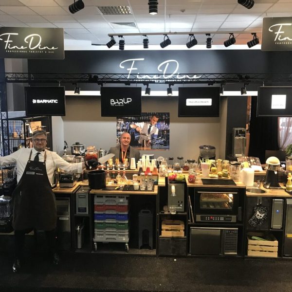 Dwóch mężczyzn w fartuchach stoi za barem szkoleniowym Bar'Up. Hendi Sweet słodkie stoisko, otoczone owocami, słoikami i sprzętem, pod szyldem Fine Dine podczas imprezy pod dachem. projekt i nadzór Tatjana Kobuszewska trksystem.com